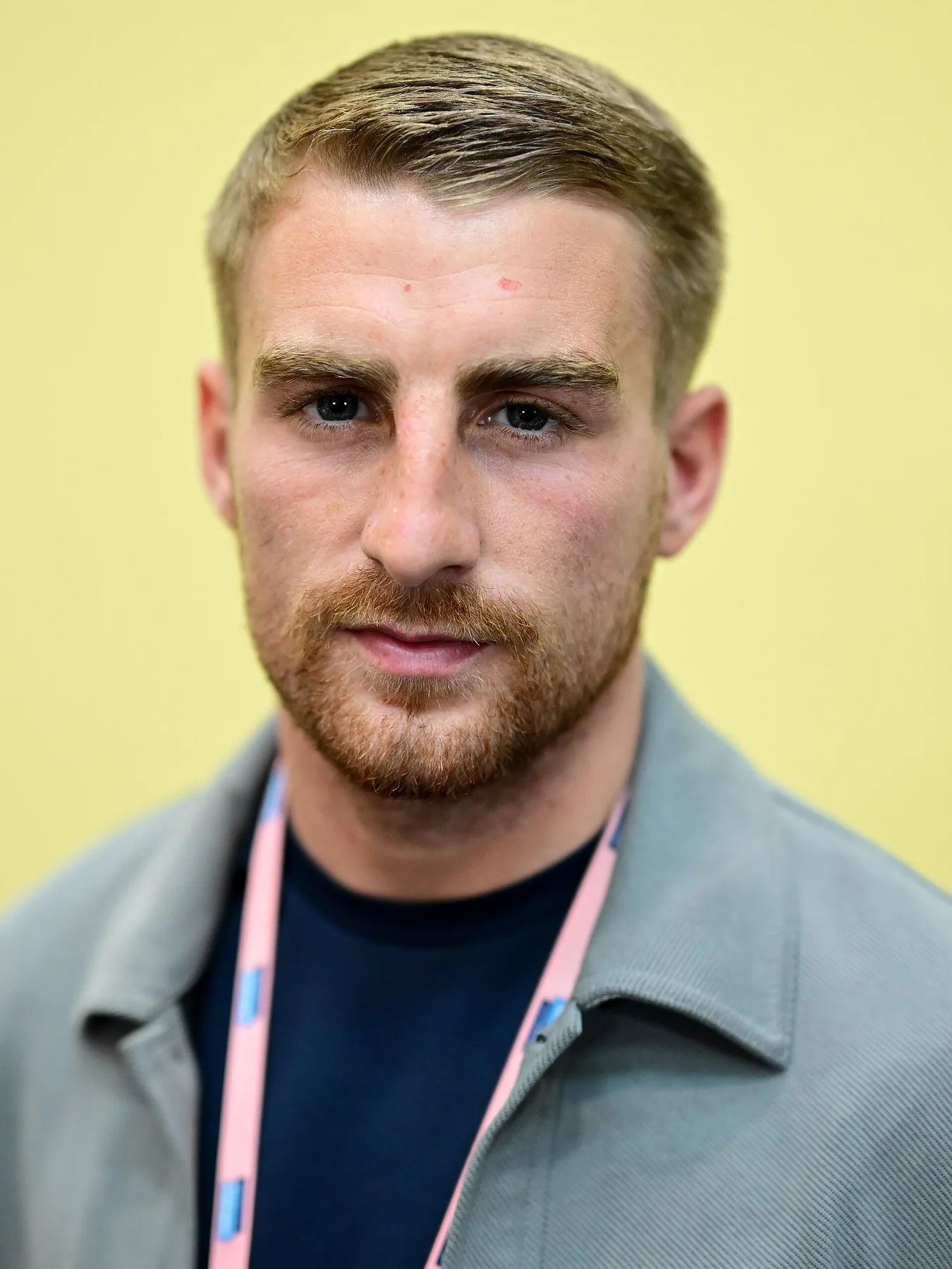 Jonathan Haggerty in a grey jacket and pink lanyard, head and shoulders against a yellow wall