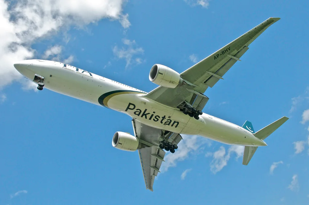 PIA Boeing 777 in Pakistan livery seen from below with landing gear down against a blue sky