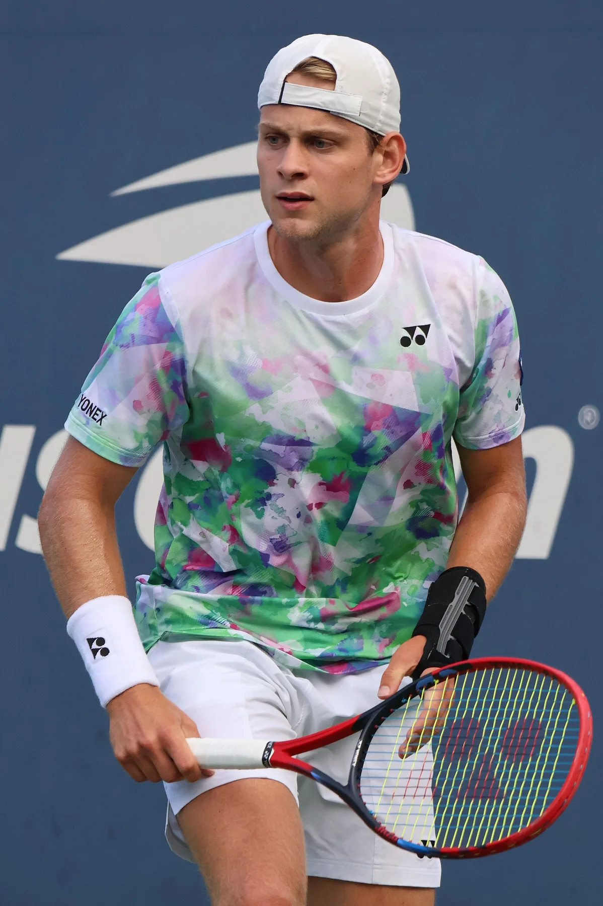 Zizou Bergs in a white cap and colourful shirt holding a red racquet during a match at the US Open