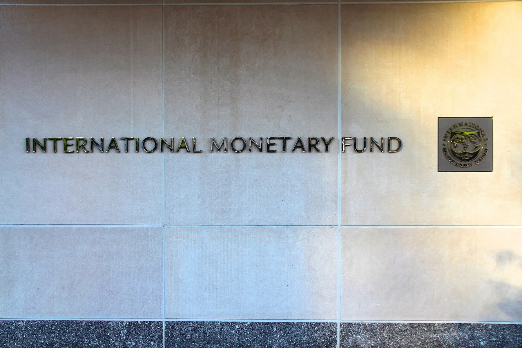 Metal lettering reading International Monetary Fund and the IMF seal on a stone wall