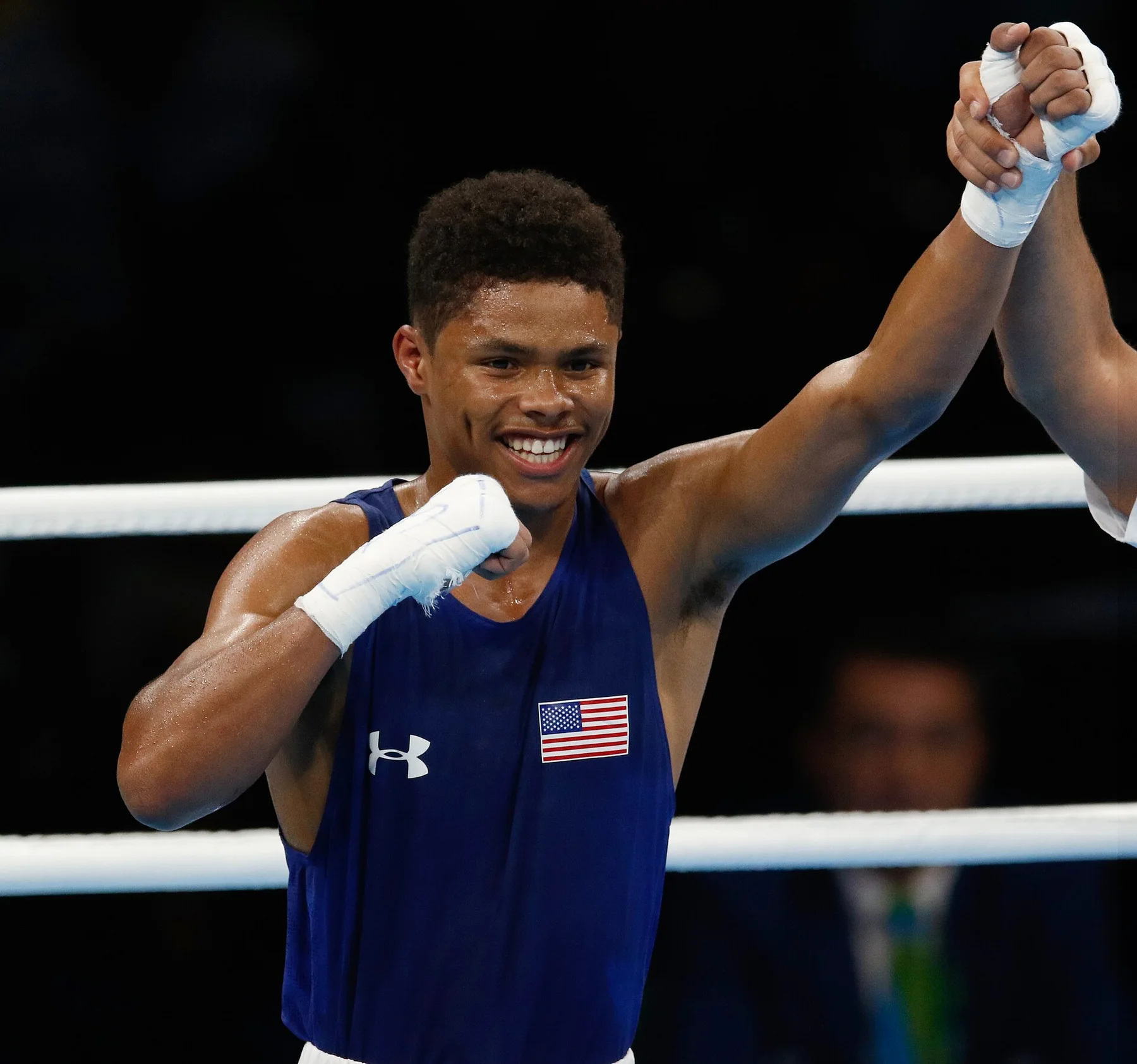 Shakur Stevenson in a blue USA vest smiles as the referee raises his arm in a boxing ring