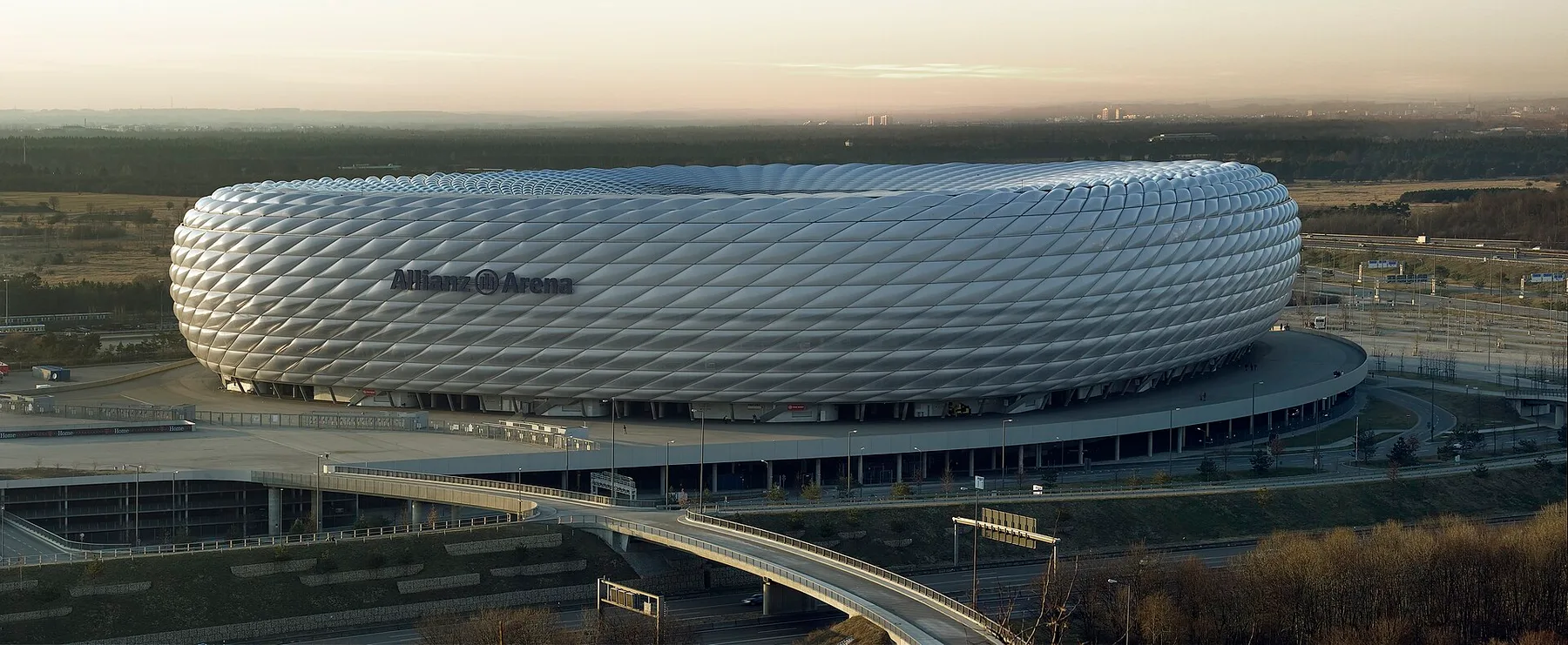 The silver diamond-panelled Allianz Arena in Munich at dusk, seen from above with its access bridges