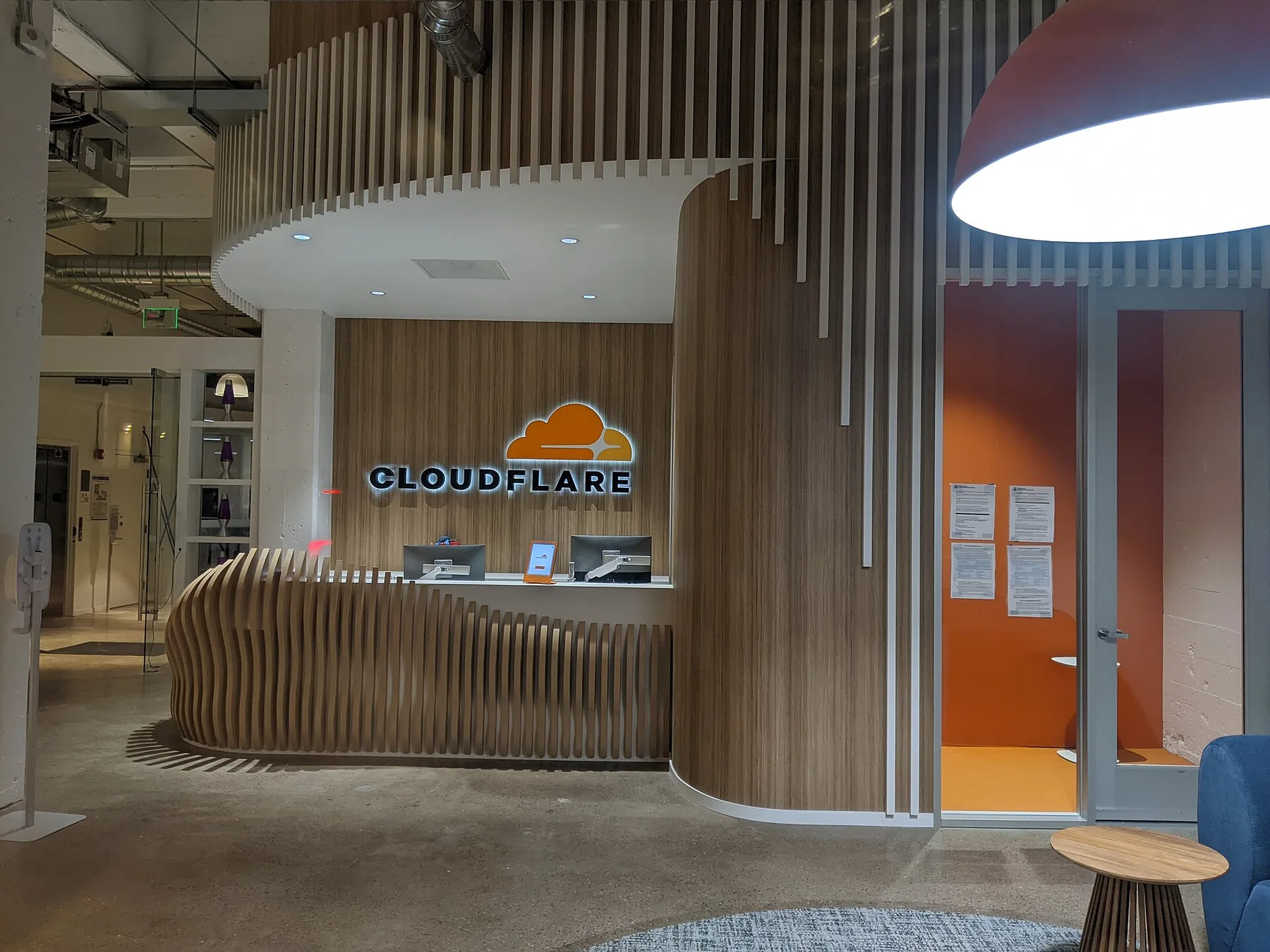 Cloudflare reception desk with the orange cloud logo lit on a wooden wall