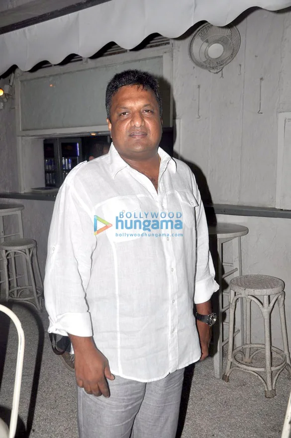 Sanjay Gupta in a white shirt standing at an indoor event with bar stools behind him