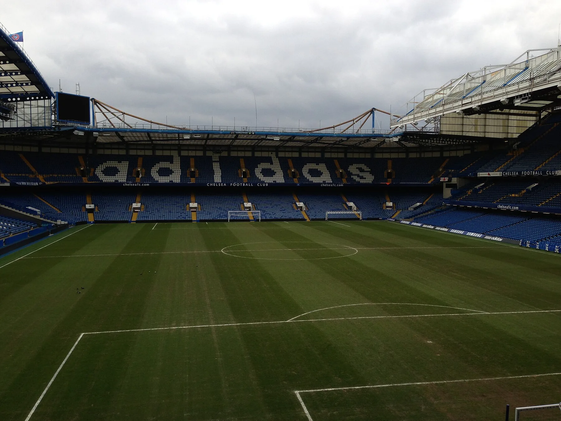 Empty Stamford Bridge pitch and blue stands with Chelsea Football Club signage on an overcast day