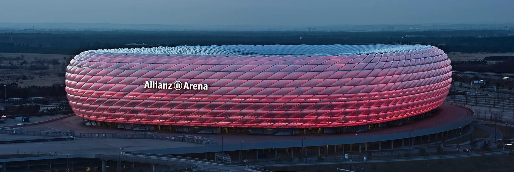 Allianz Arena in Munich lit up red at dusk, its name in white letters on the curved facade