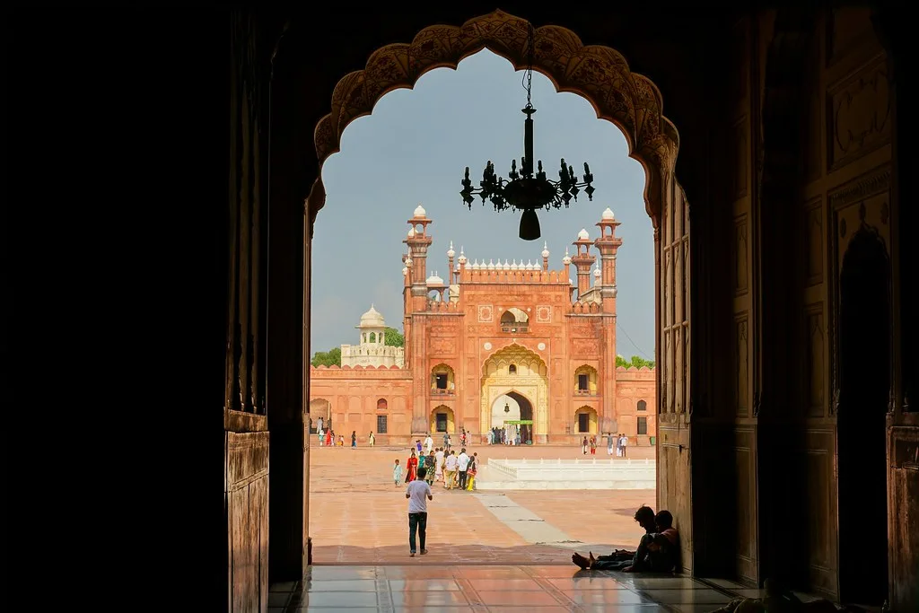 Badshahi Mosque courtyard and gateway in Lahore seen through a carved arch, with visitors walking