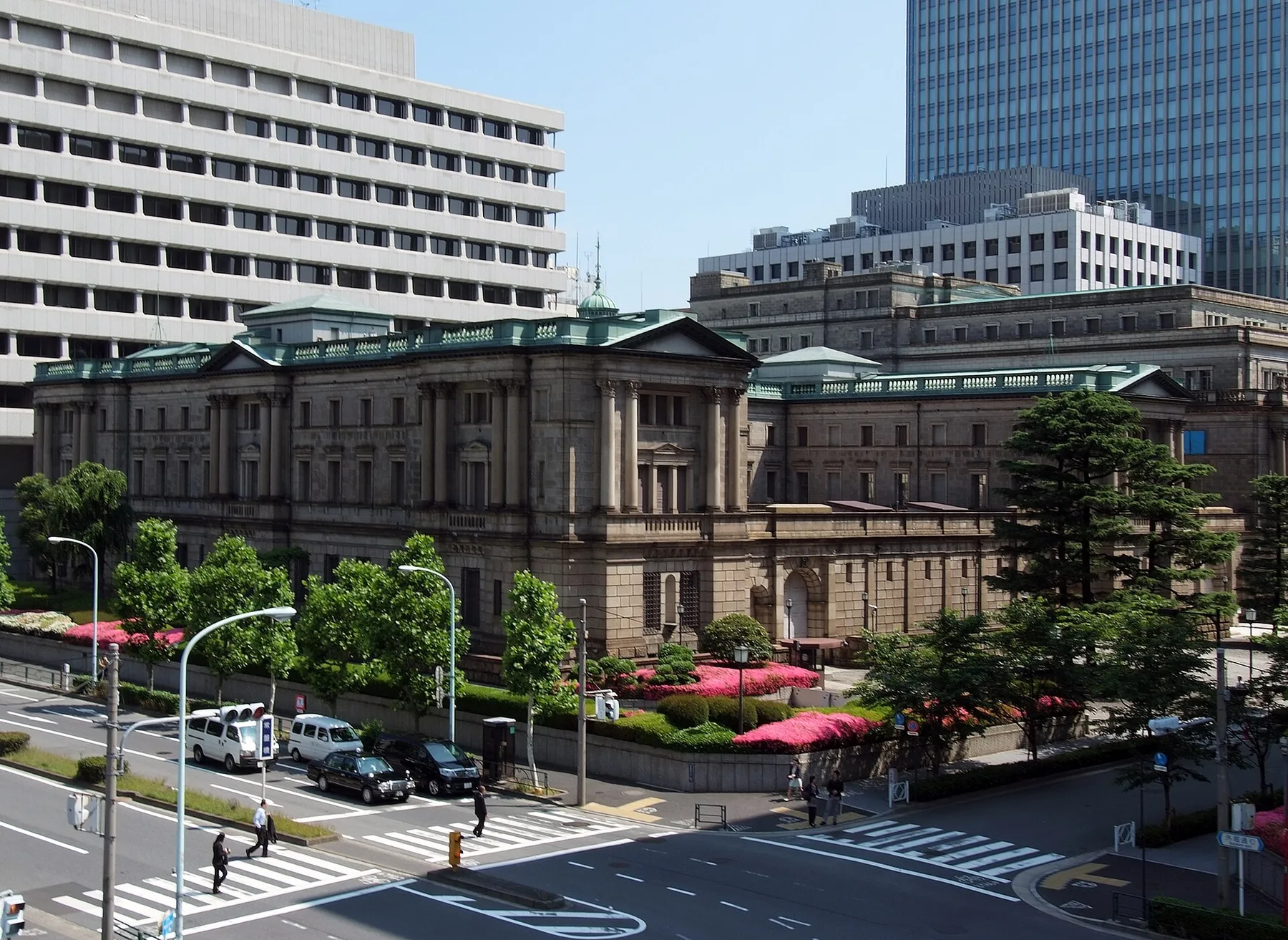 Stone Bank of Japan head office building in Tokyo behind trees, with a street crossing in front