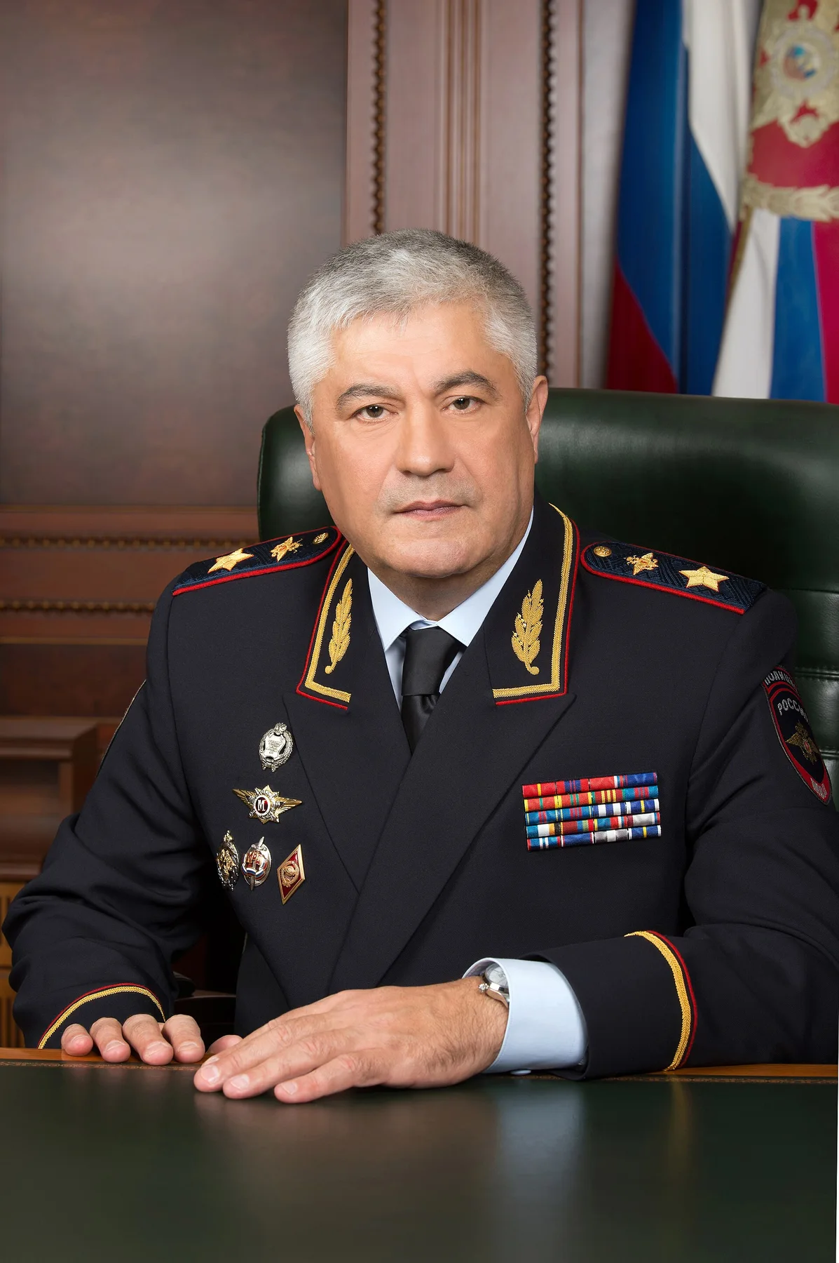 Russian Interior Minister Vladimir Kolokoltsev in uniform seated at a desk beside the Russian flag
