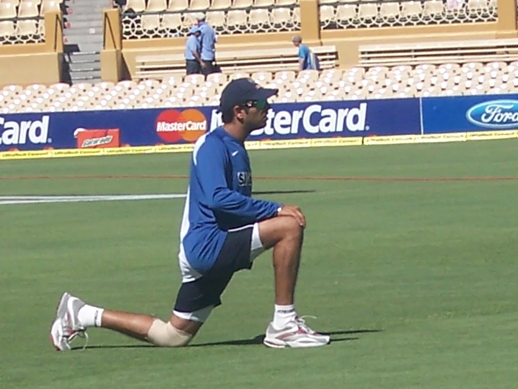 Yuvraj Singh in a blue India training top stretching on one knee on a cricket outfield