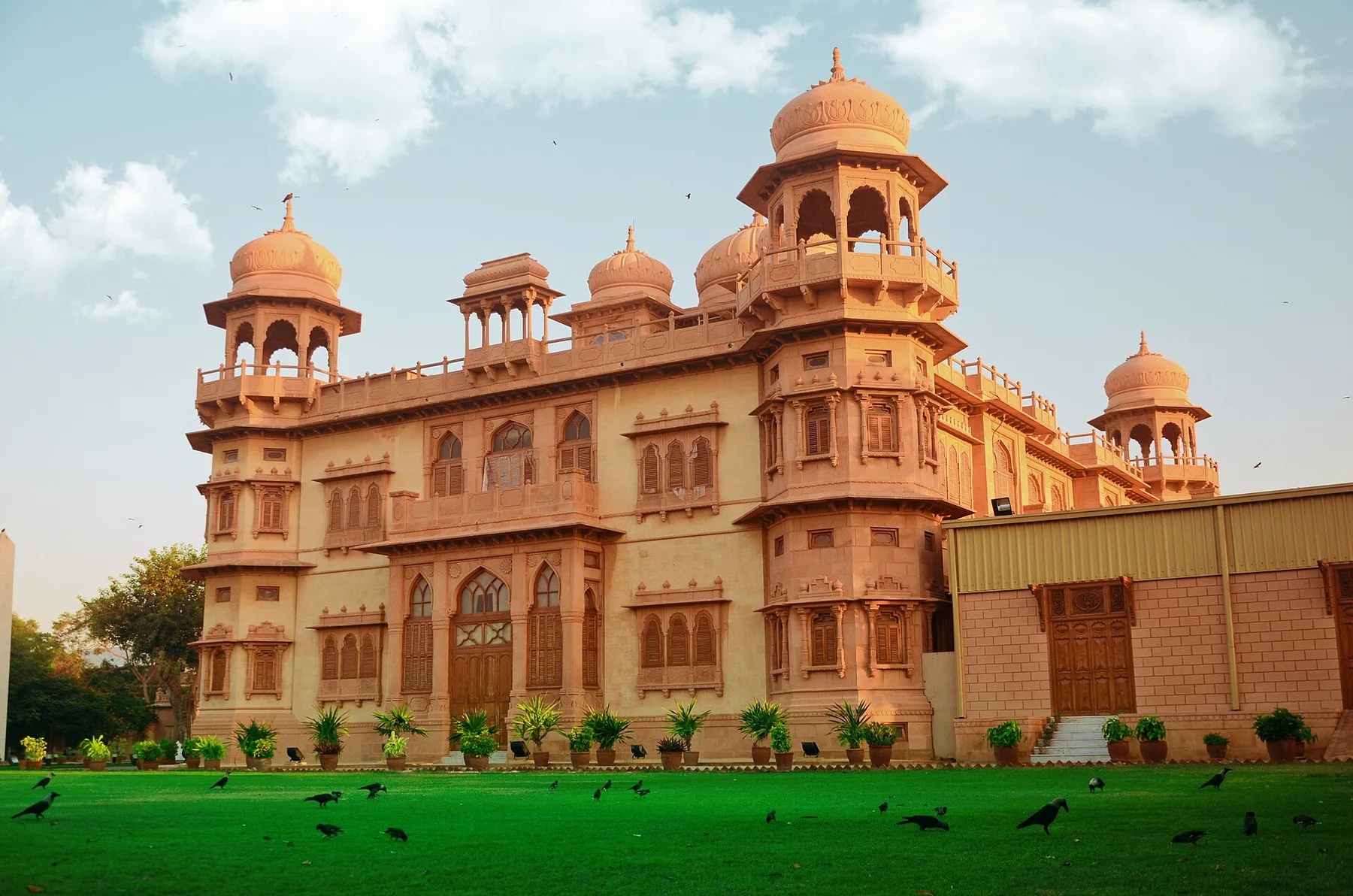 Pink stone Mohatta Palace in Clifton, Karachi, with domed towers above a green lawn and crows