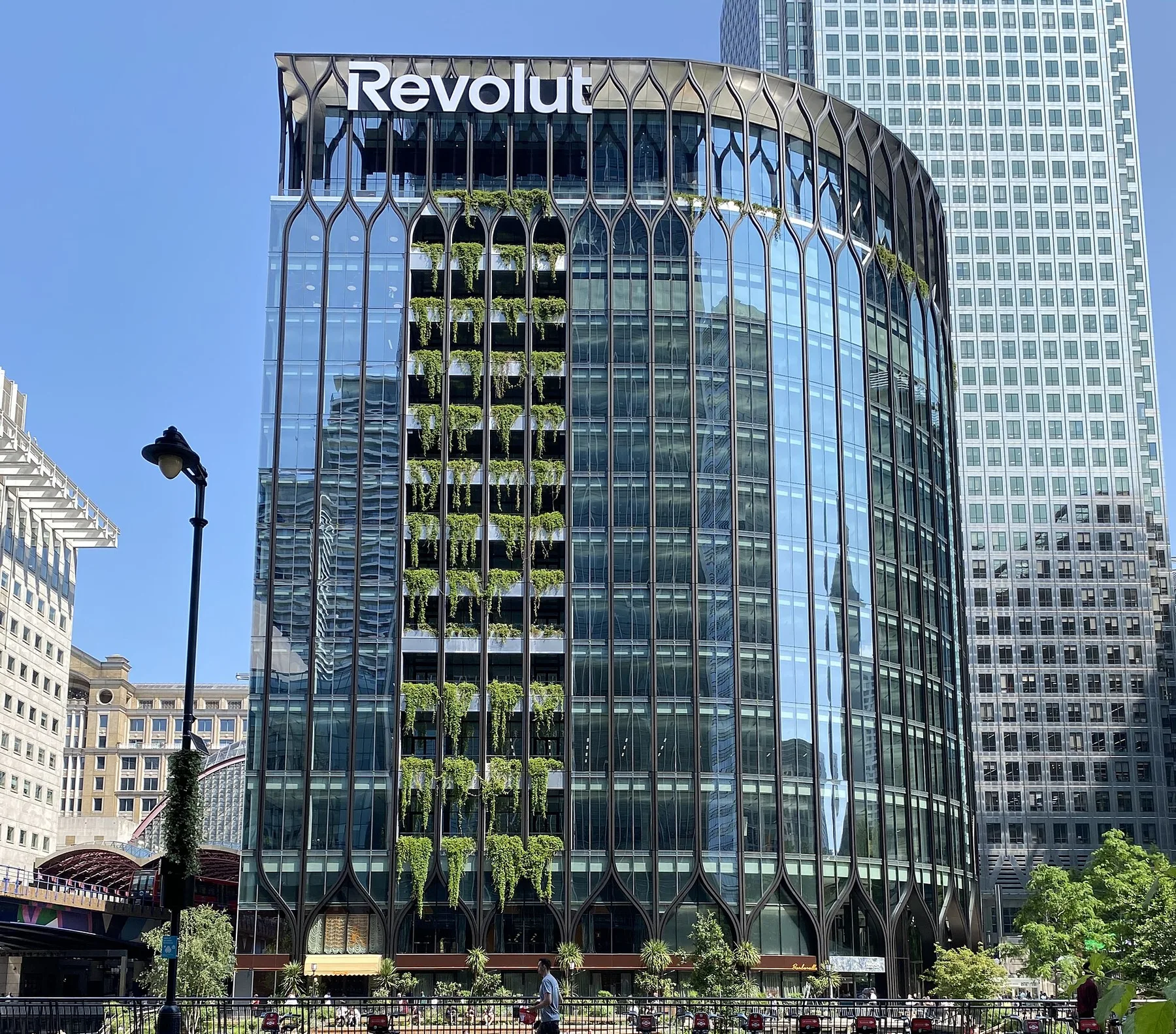 Glass office tower topped by a large Revolut logo, with hanging plants down its curved facade