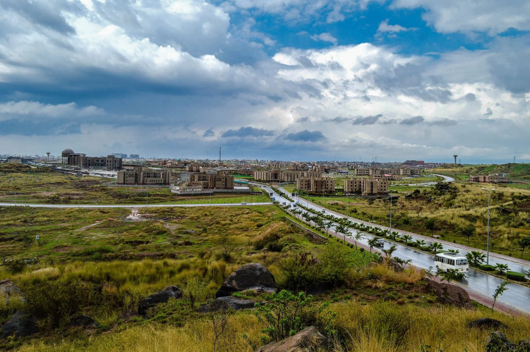 NUST campus buildings in Islamabad H-12 seen from a hill under cloudy sky, a road and bus in front
