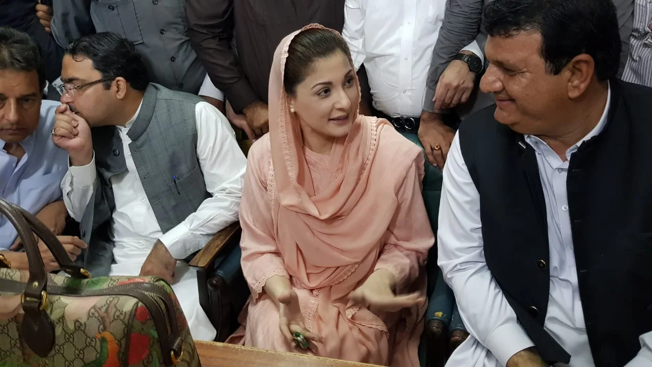Maryam Nawaz Sharif in a pink dupatta, seated and talking among party colleagues in a crowded room