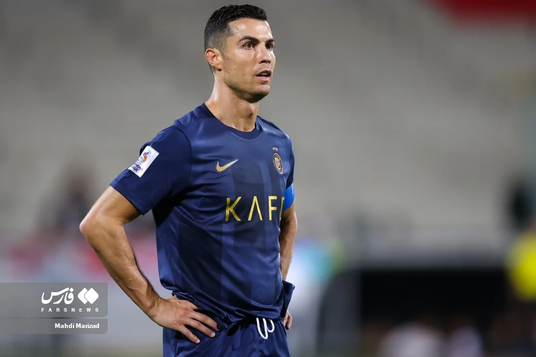 Cristiano Ronaldo in a navy Al-Nassr kit with captain armband, hands on hips in a stadium