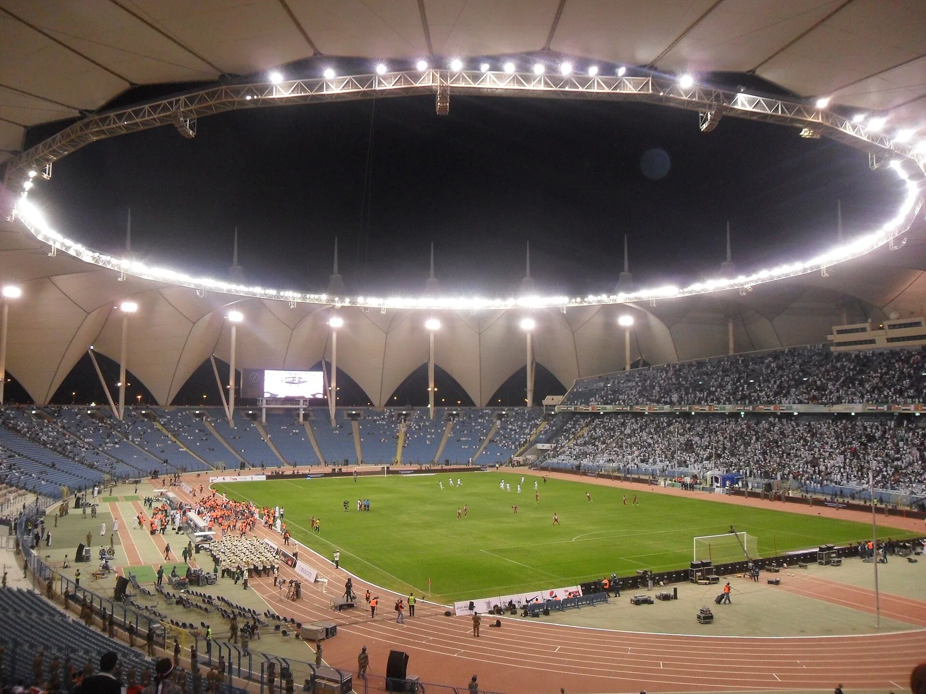 Floodlit King Fahd stadium in Riyadh with its tent roof, a football match under way and crowds in the stands