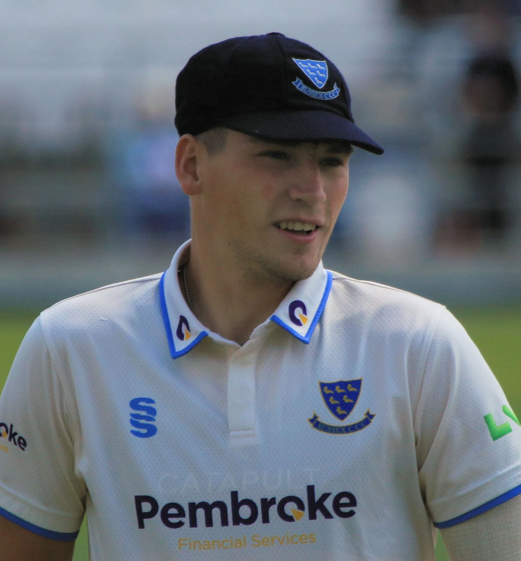 Henry Crocombe in a Sussex cap and cream playing shirt on the field during a county match
