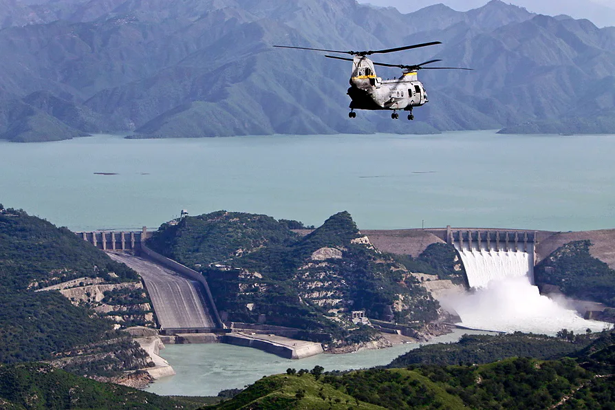 Tarbela Dam reservoir and spillway releasing water, with a helicopter flying above the hills
