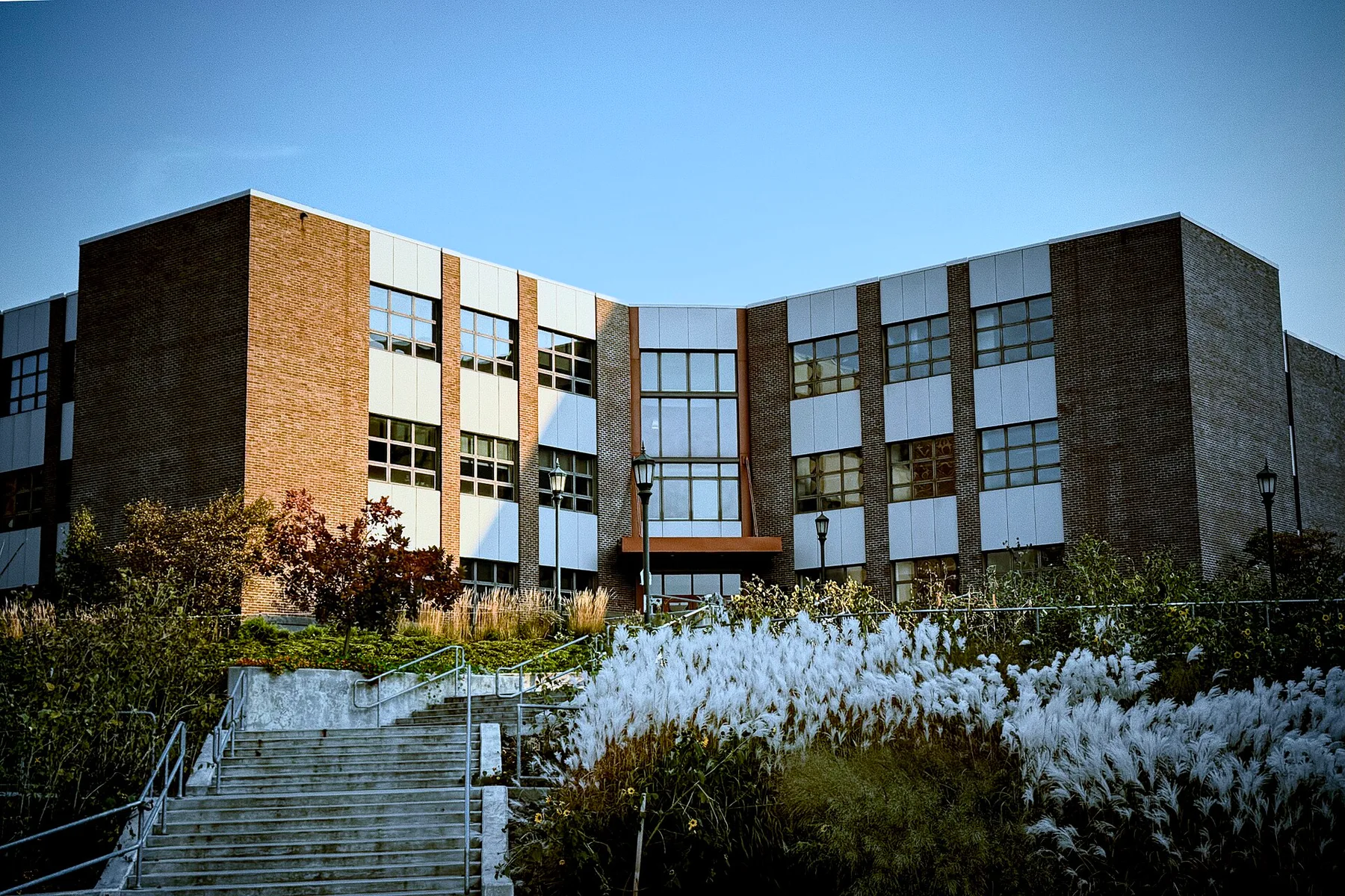 Brick and glass Aiken Center building at the University of Vermont, with steps and pale ornamental grasses