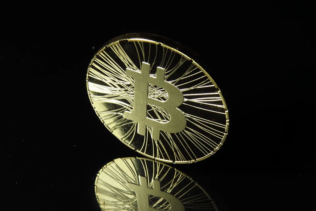 Gold-coloured physical bitcoin coin standing on a black reflective surface