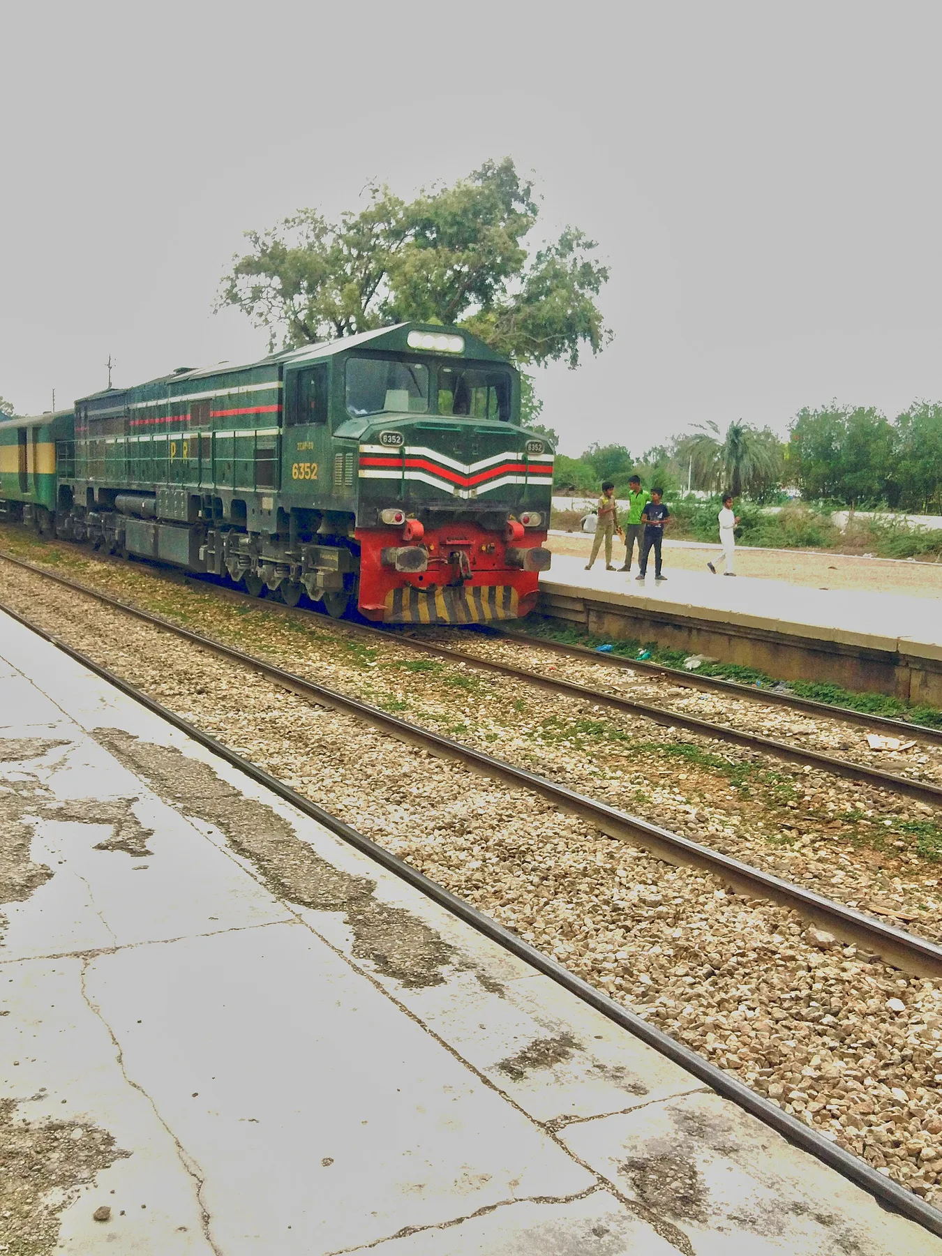 Green Pakistan Railways diesel locomotive pulling a passenger train past a station platform