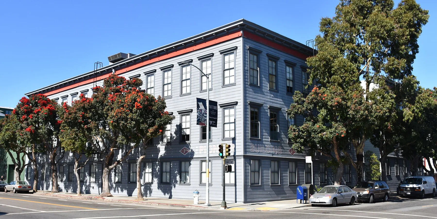 Grey three-storey Pioneer Building in San Francisco, an OpenAI office, with red-flowering trees outside