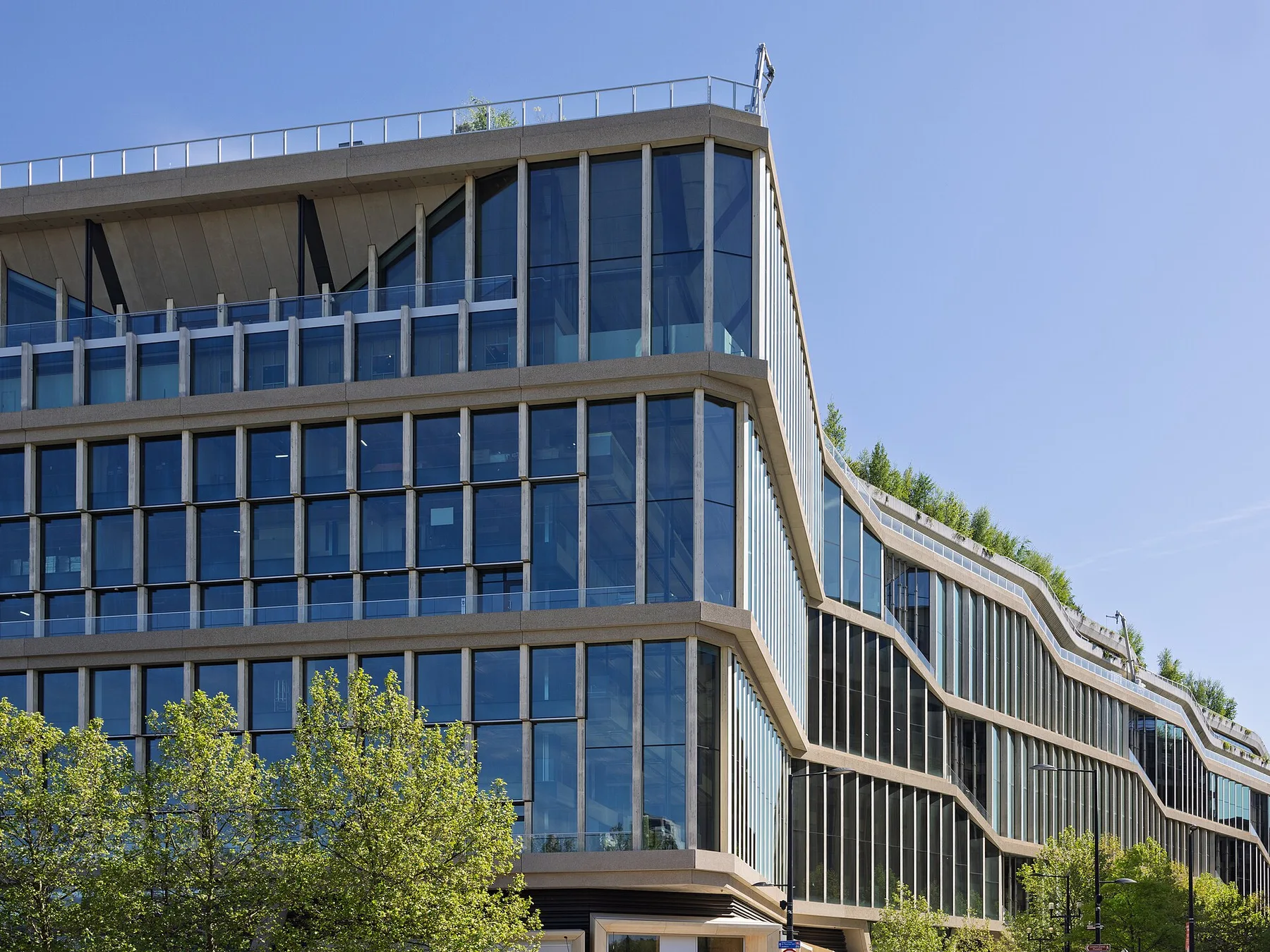 Glass-fronted Google office building with stepped floors and rooftop trees against a blue sky