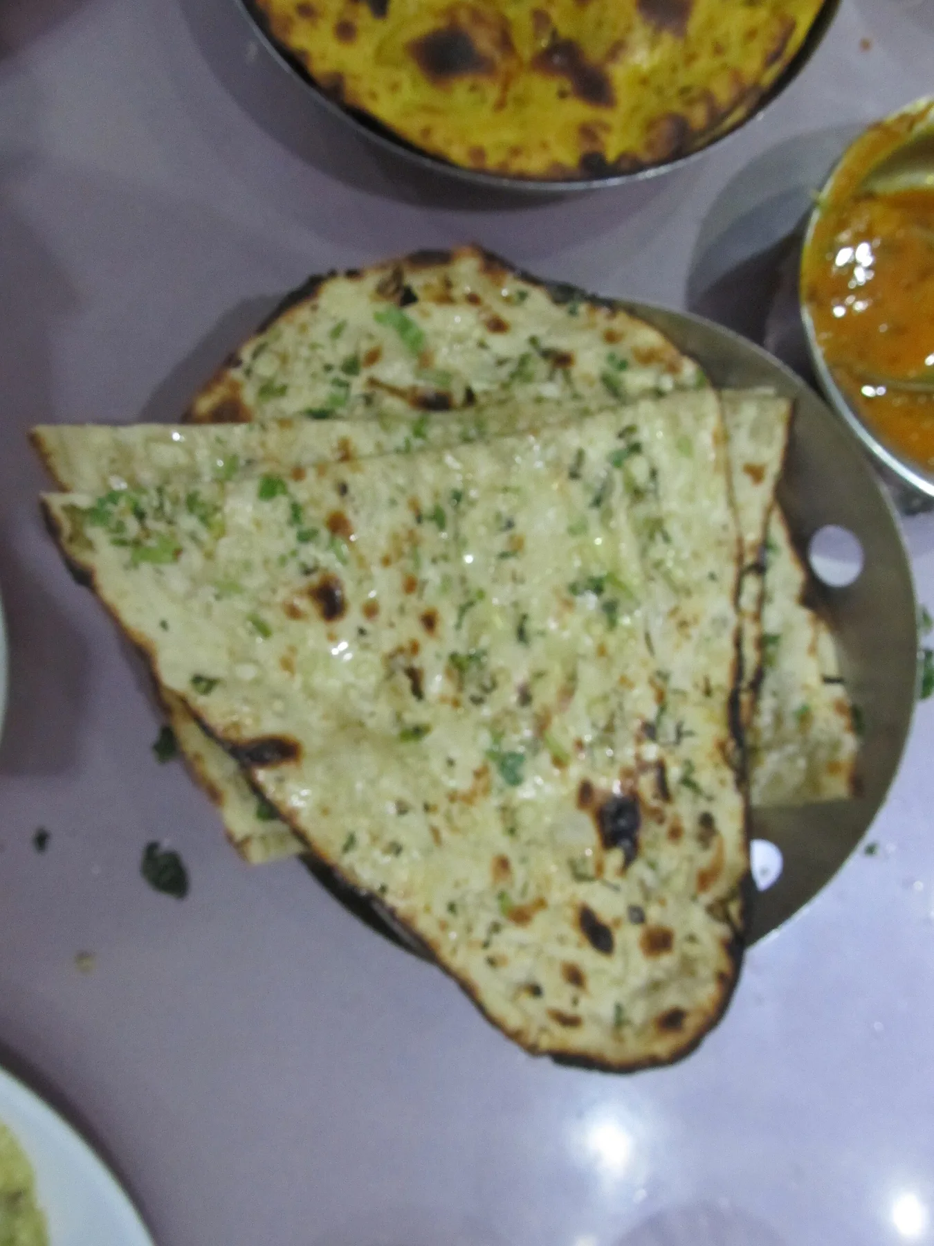 Folded tandoori naans topped with herbs on a steel plate beside a bowl of curry