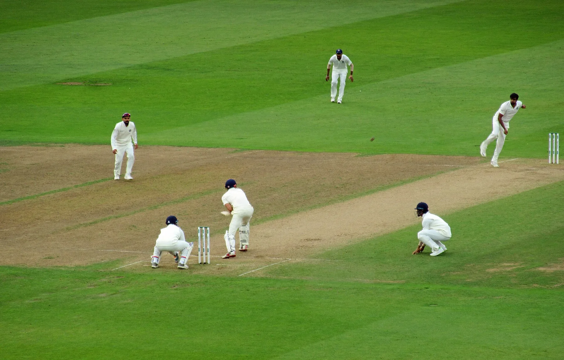 India fielders in white surround the batter as a fast bowler delivers during a Test match