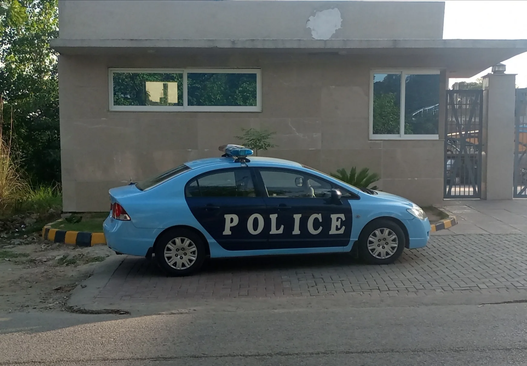 Light blue Islamabad police car parked outside a gated building