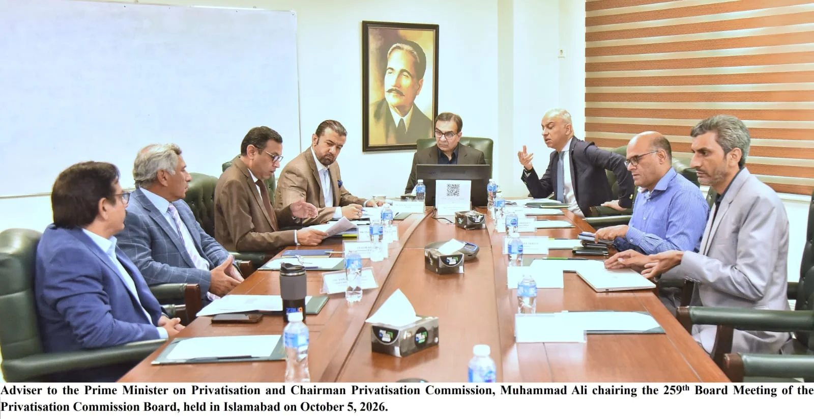 Privatisation Commission Board members around a conference table in Islamabad, a portrait of Allama Iqbal behind