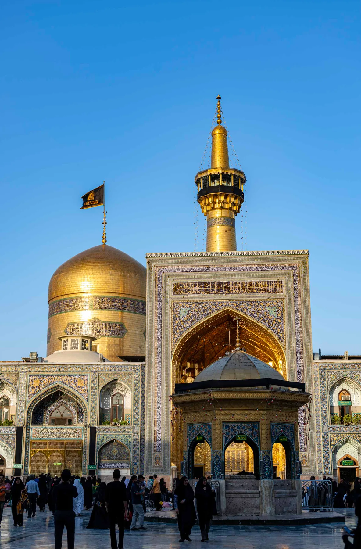 Golden dome and tiled minaret of a shrine in Iran, with pilgrims walking across the courtyard