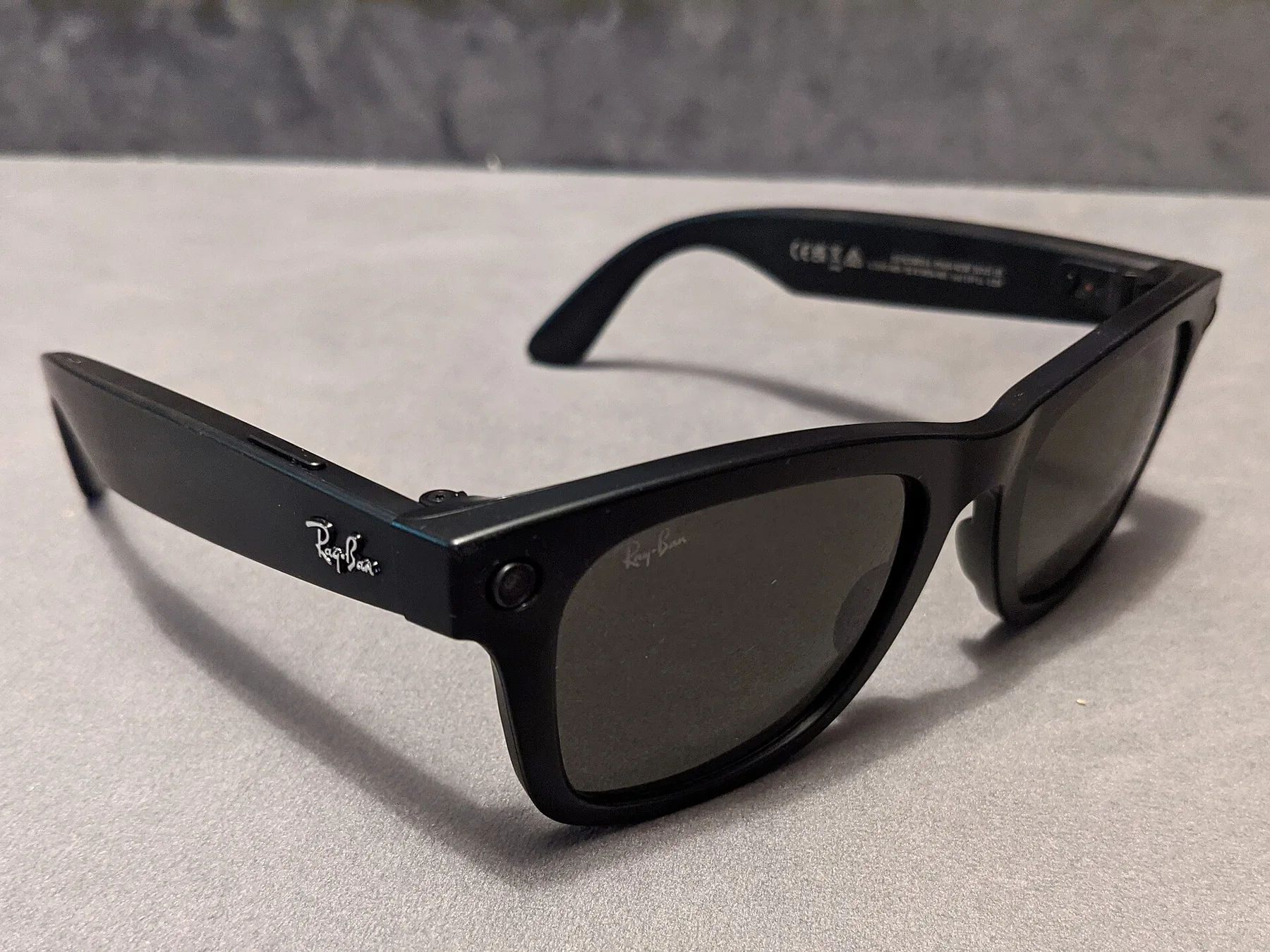 Black Ray-Ban Meta smart glasses with a small camera lens on the frame, resting on a grey table